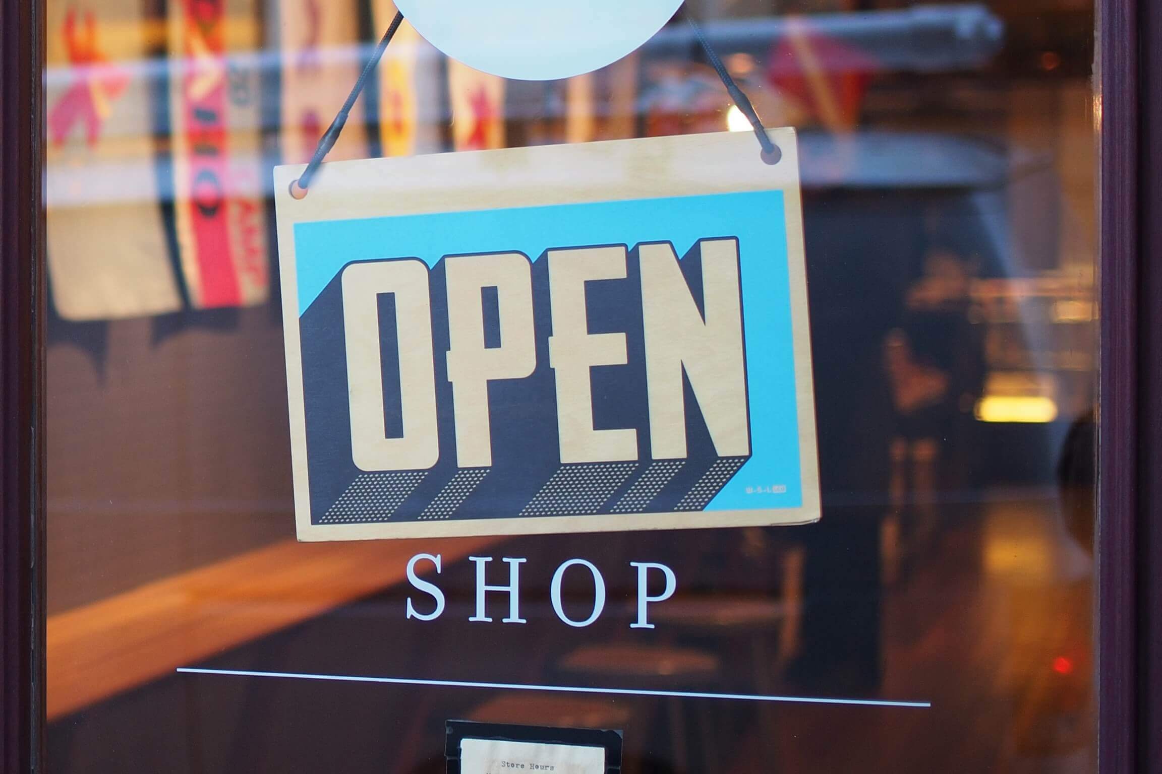 A blue and yellow "OPEN" sign hangs on a glass door, with the word "SHOP" printed below it—inviting freelancers inside. The shop’s welcoming interior can be seen through the glass.